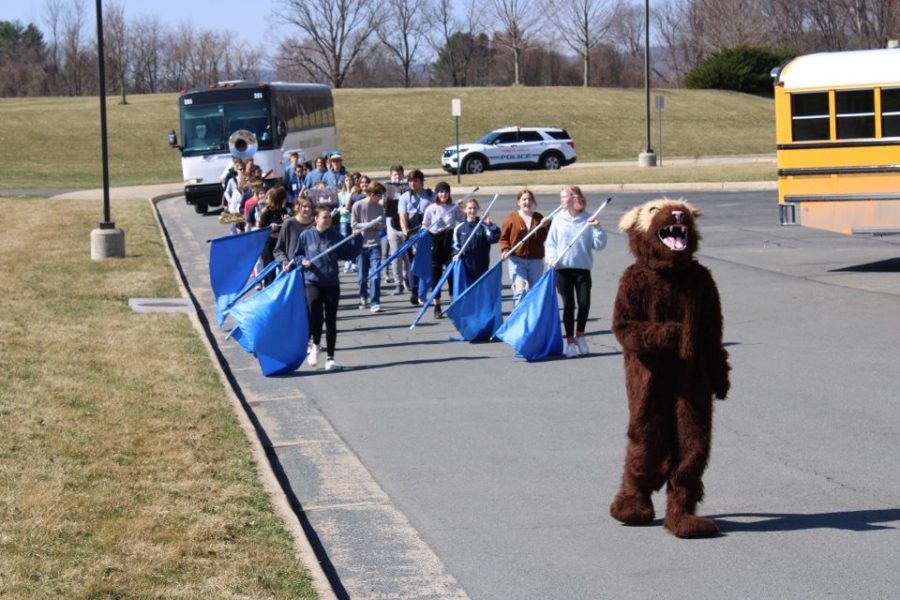 Walter Wolverine leads the marching band ahead of the bus taking Woodgroves girls basketball team to the state championship.
