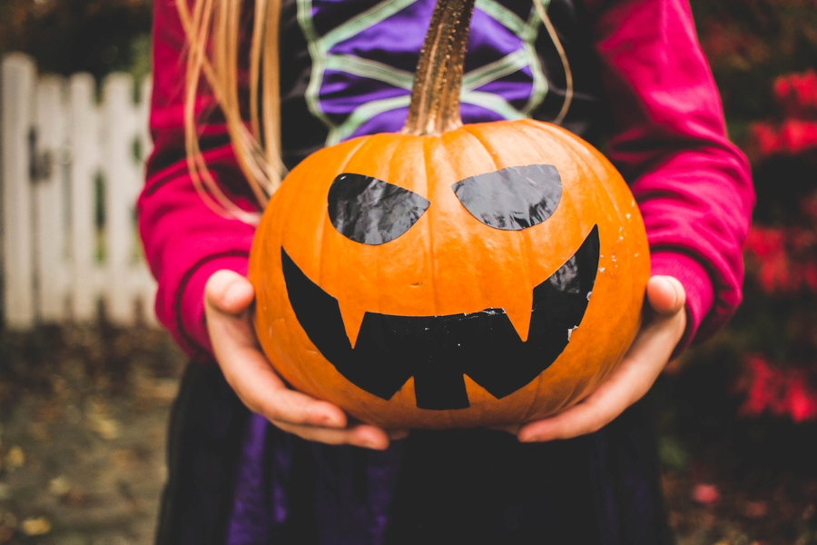 Child holding a more modernized version of a jack-o-lantern, with the face painted on rather than carved out.
